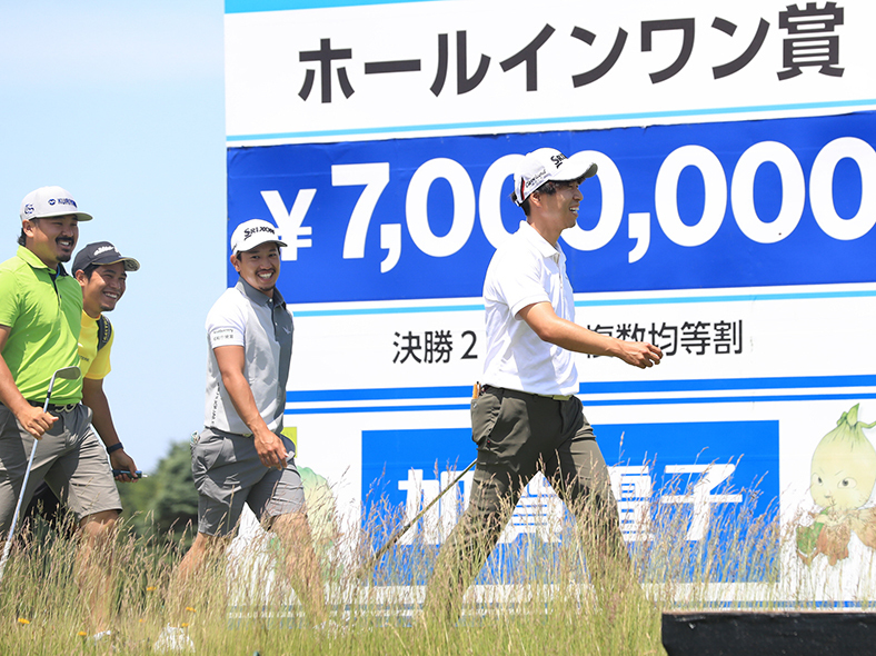 １６番パー３のティーグラウンドに立つ賞金７００万円のボード横を通り過ぎる道産子の佐藤（右）とホストプロの植竹（右から２人目）