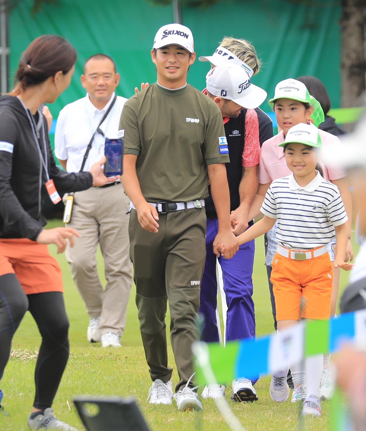 エスコートキッズと一緒にスタートの1番ホールに入場する片岡(中央)