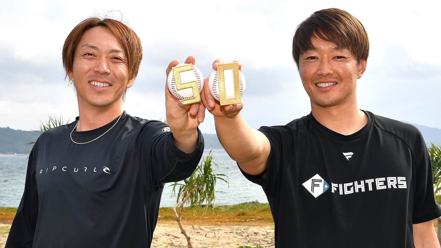 今季もともに５０試合登板を目指す宮西（左）と玉井のリリーフコンビが、沖縄・名護の砂浜をバックに満面の笑みを見せる（撮影・桜田史宏）