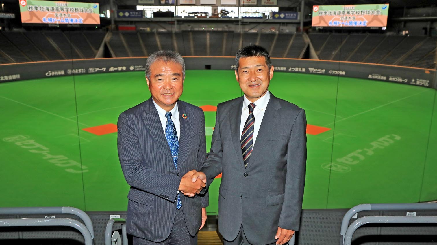 札幌ドームで握手する道高野連の坂本会長（右）と山川札幌ドーム社長
