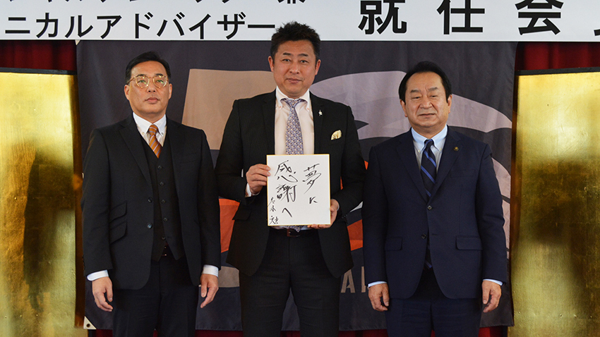 就任会見でスローガンの「夢に感謝へ」を色紙にしたためた岩本氏（中央）。左は板東美唄市長、右は荘司球団代表